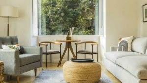 A vibrant dog park bathed in sunlight features abundant greenery with mature trees, offering ample shade for leisurely outdoor activities. In the distance is a well-equipped playground that presents an additional activity area. An inviting picnic table spreads out nearby, ideal for enjoying meals al fresco or taking relaxing breaks from play. A neatly-placed trash bin aids in maintaining the park's cleanliness for everyone's enjoyment. Dominating the scene is a generously wide dirt path gracefully curving through the expanse of grass, promising exploratory walks and lively fetch games.